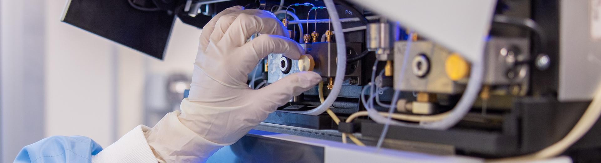 Eine Person mit Schutzhandschuhen und Laborkittel bedient ein Gerät in einem Labor