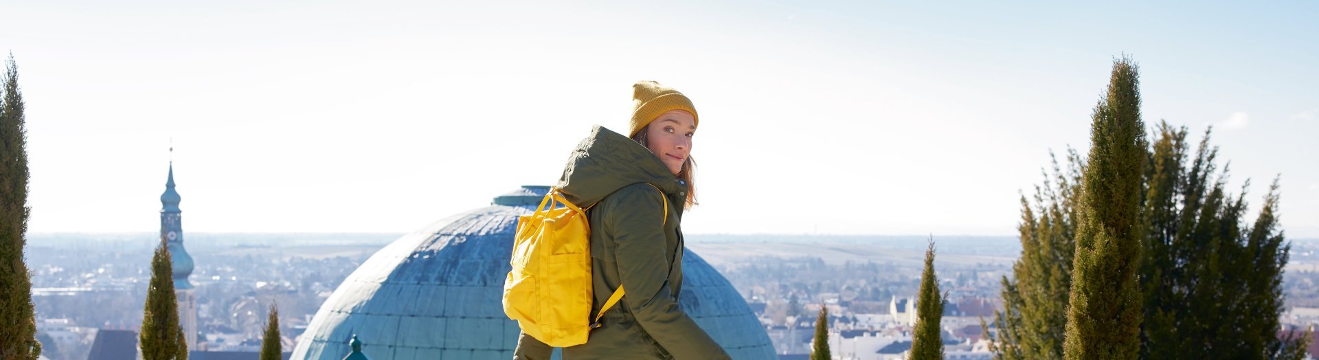 Dame mit gelbem Rucksack und schmalen hohen Bäumen 
