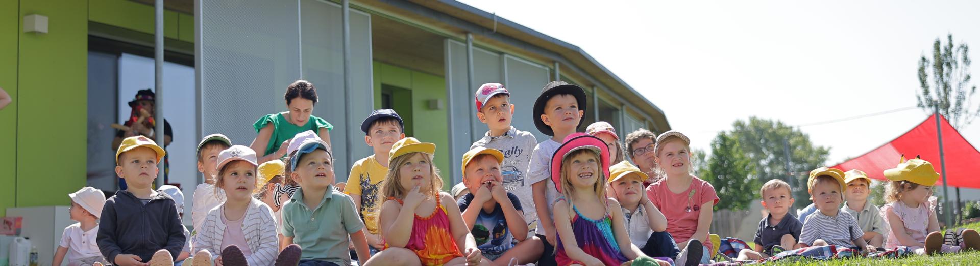 Kindergartenkinder einer Gruppe sitzen am Rasen im Garten