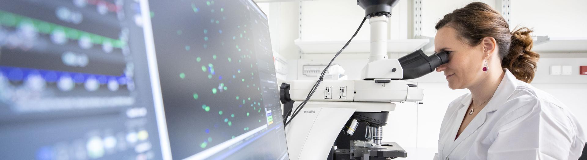 Forscherin beim Mikroskopieren mit großen Bildschirm vom Vordergrund