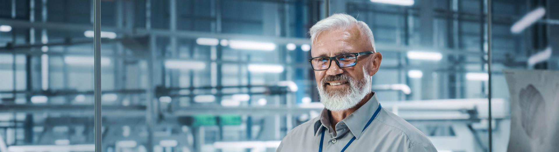 reifer Mann in Produktionshalle mit Laptop in der Hand
