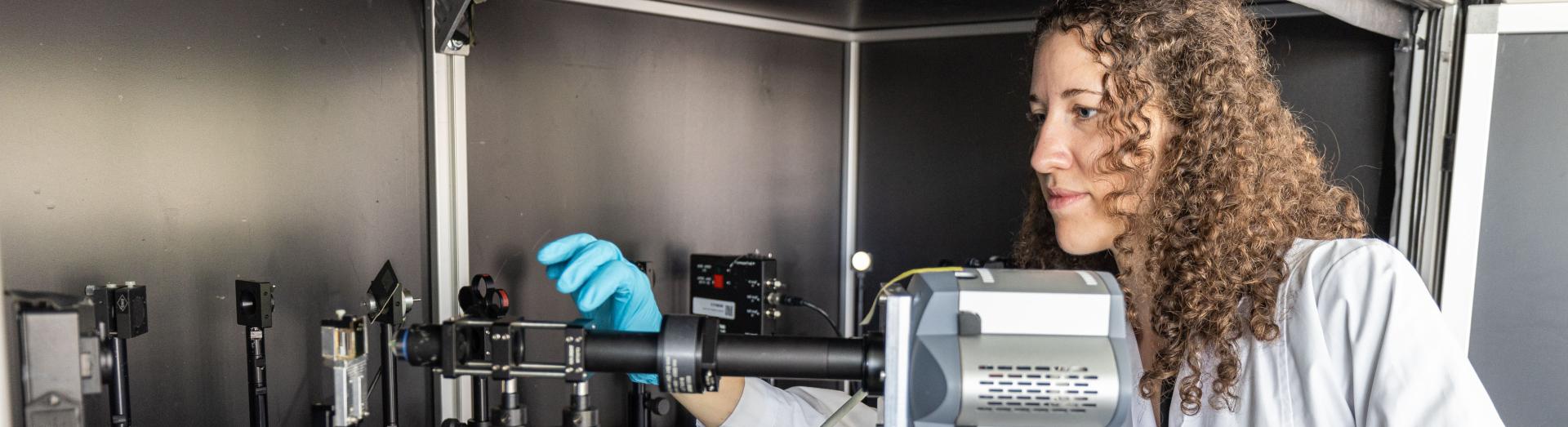 Forscherin in weißem Mantel und mit türkisen Handschuhen bedient ein elektronisches Gerät für präzische Messungen