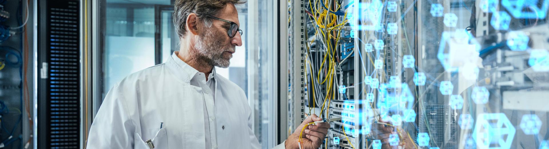 Älterer männlicher Techniker beim Einstecken von Glasfaserkabeln im Rechenzentrum