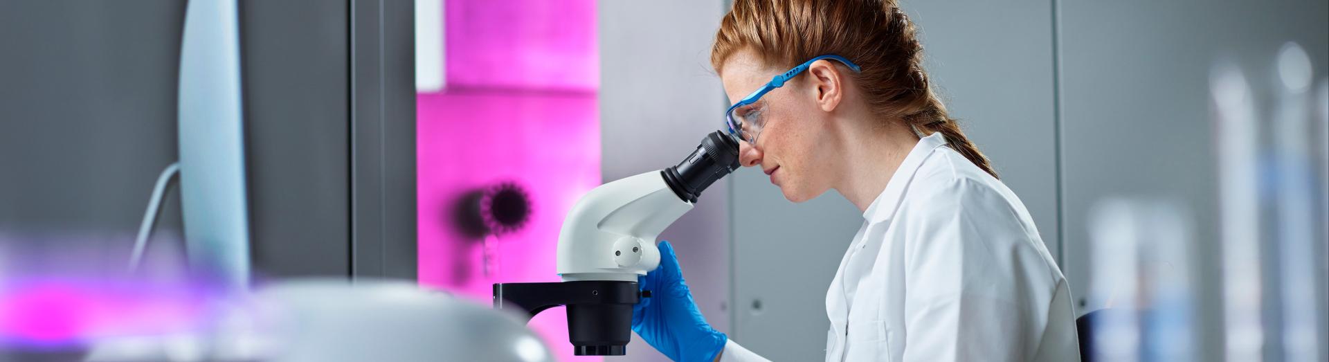 Dame im weißen Labormantel sitzt am Mikroskop