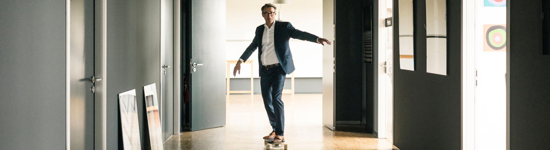 Auf Skateboard rollender Business Man in einem Büro-Gang 