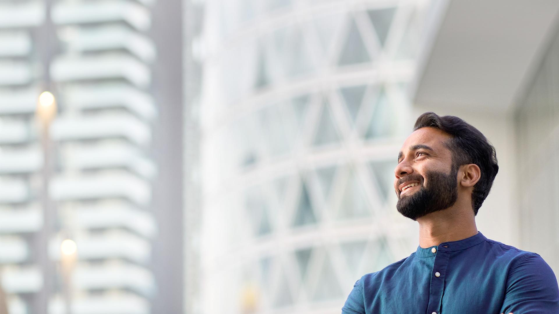 Bärtiger Mann mit verschränkten Händen steht vor Hochhäusern