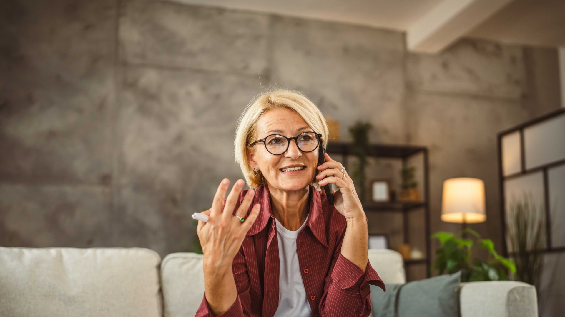 Elderly lady sits on sofa, works from home and talks on the phone