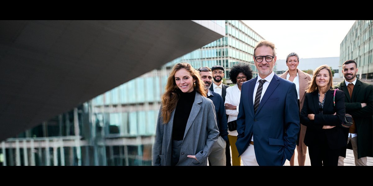 Personengruppe in Anzug steht vor modernen Bürogebäuden mit Glasfassade