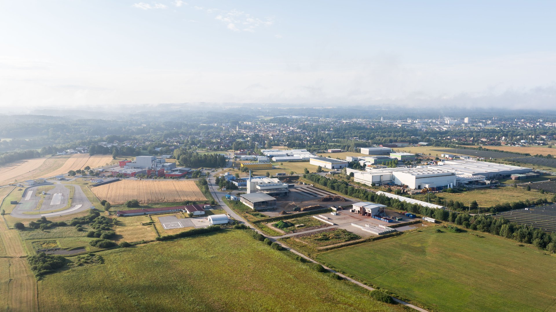 Drohnenansicht von einem Betriebsgelände im Vordergrund mit einer Stadt im Hintergrund