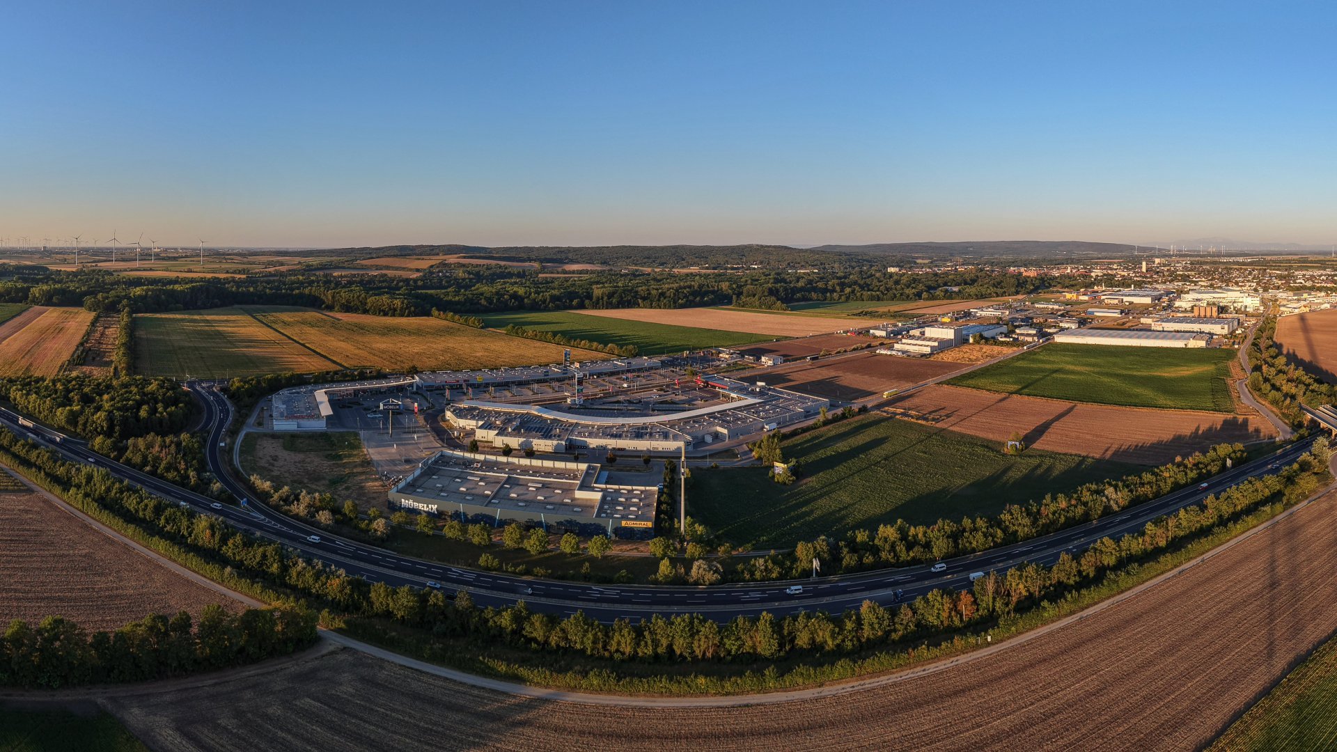 Drohnenansicht Fachmarktzentrum, Autobahn A4 mit Feldern, Wirtschaftsparkareal und Stadt Bruck an der Leitha im Hintergrund