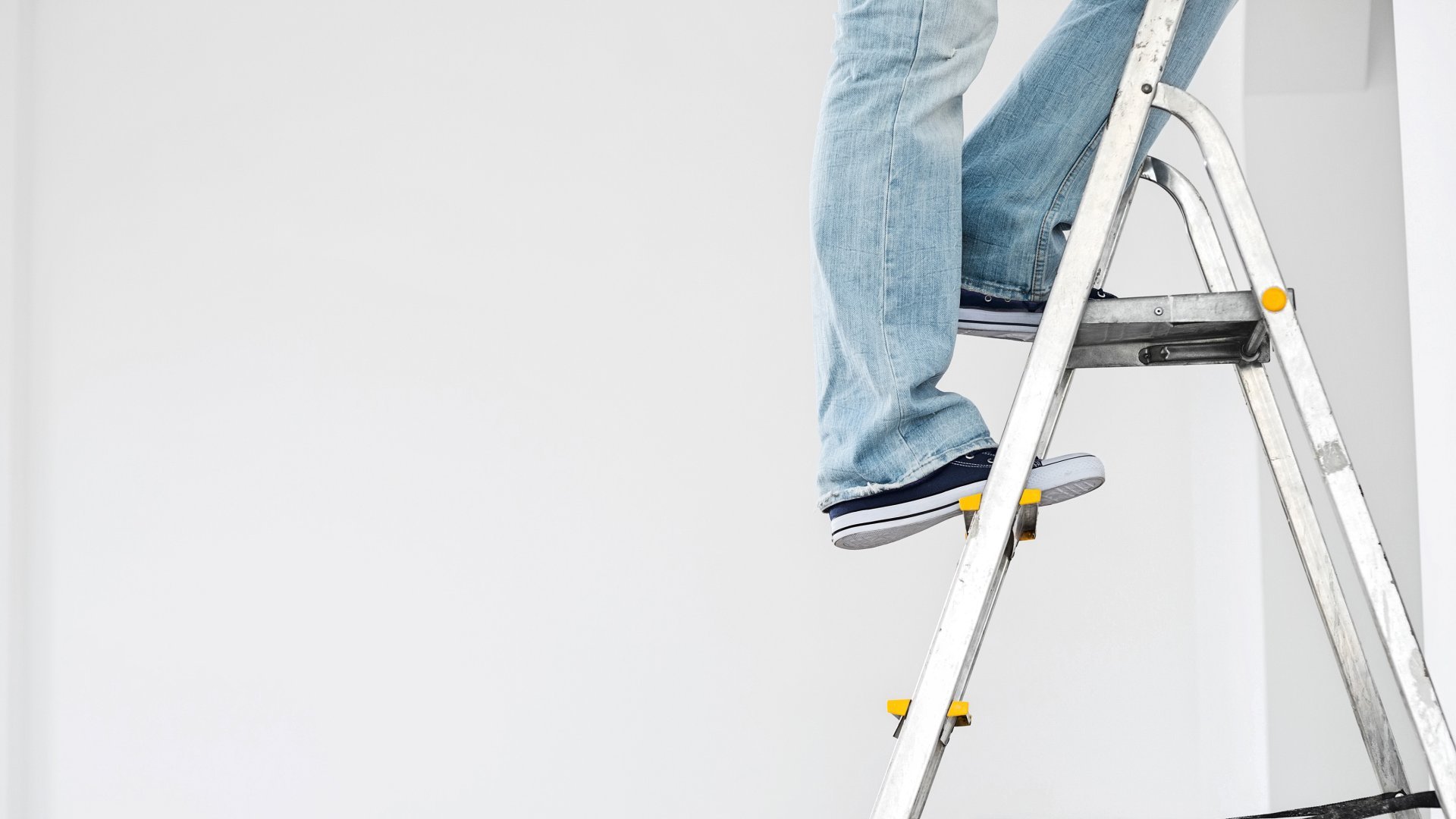 Aluleiter mit Person in Jeans und Sneakers auf den oberen Stufen