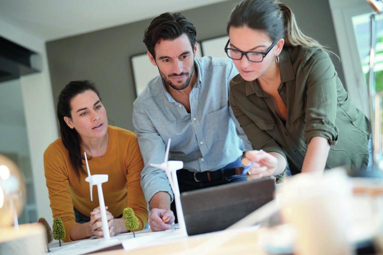 Besprechungsszene mit drei Personen und kleinen Windrädern am Tisch
