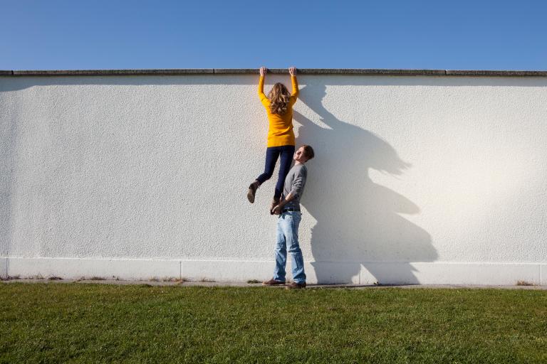 Bursch macht Mädchen eine Räuberleiter vor weißer Wand