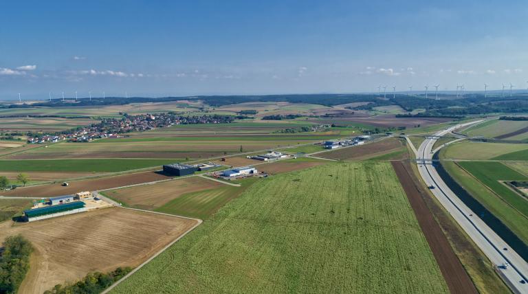 Luftbild Wirtschaftspark Wilfersdorf-Mistelbach mit freien Feald im Vordergrund, Unternehmensgebäuden und Autobahn