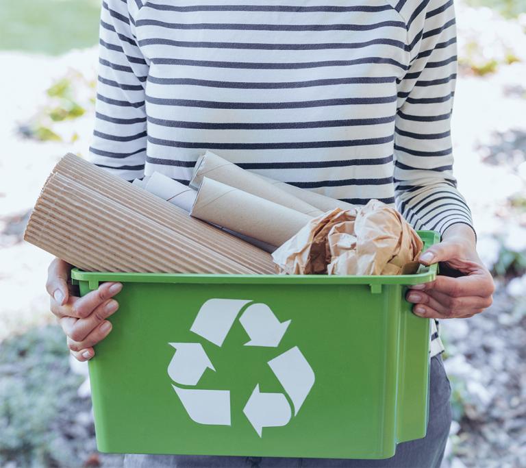 Person mit Aufbewahrungsbox inklusive Kreislaufsymbol gefüllt mit Papier in der Hand