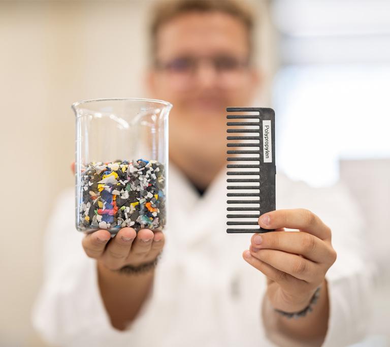 Junger Mann hällt Polypropylen & einen Kamm in seinen Händen 