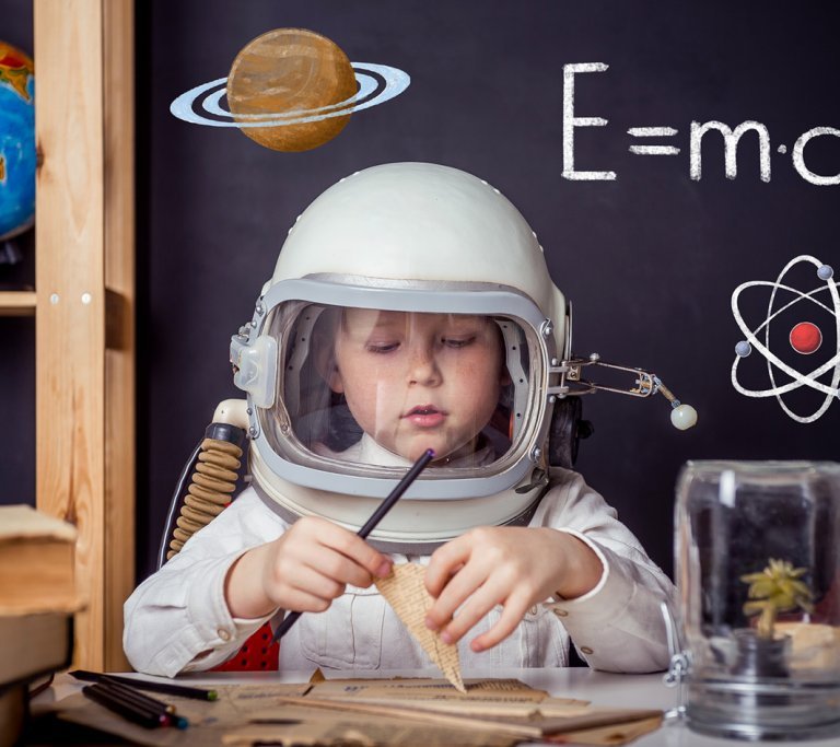 Junge sitzt an Schreibtisch mir Austronautenhelm