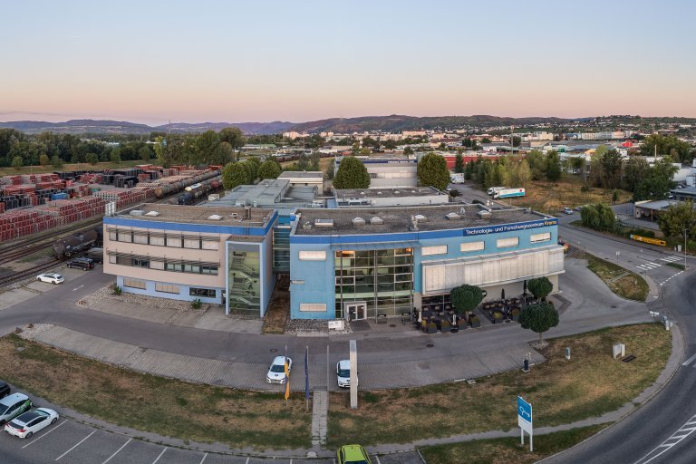 Blaues Gebäude neben Bahngleisen und der Stadt Krems im Hintergrund