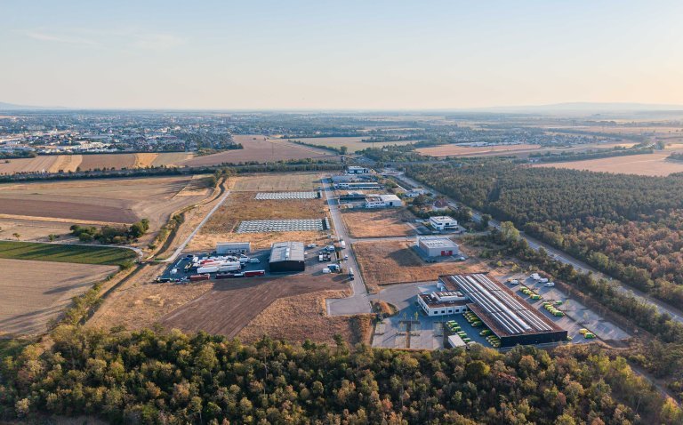 Drohnenaufnahme eines Wirtschaftspark Areals neben einer Straße und Föhrenwäldern und Feldern