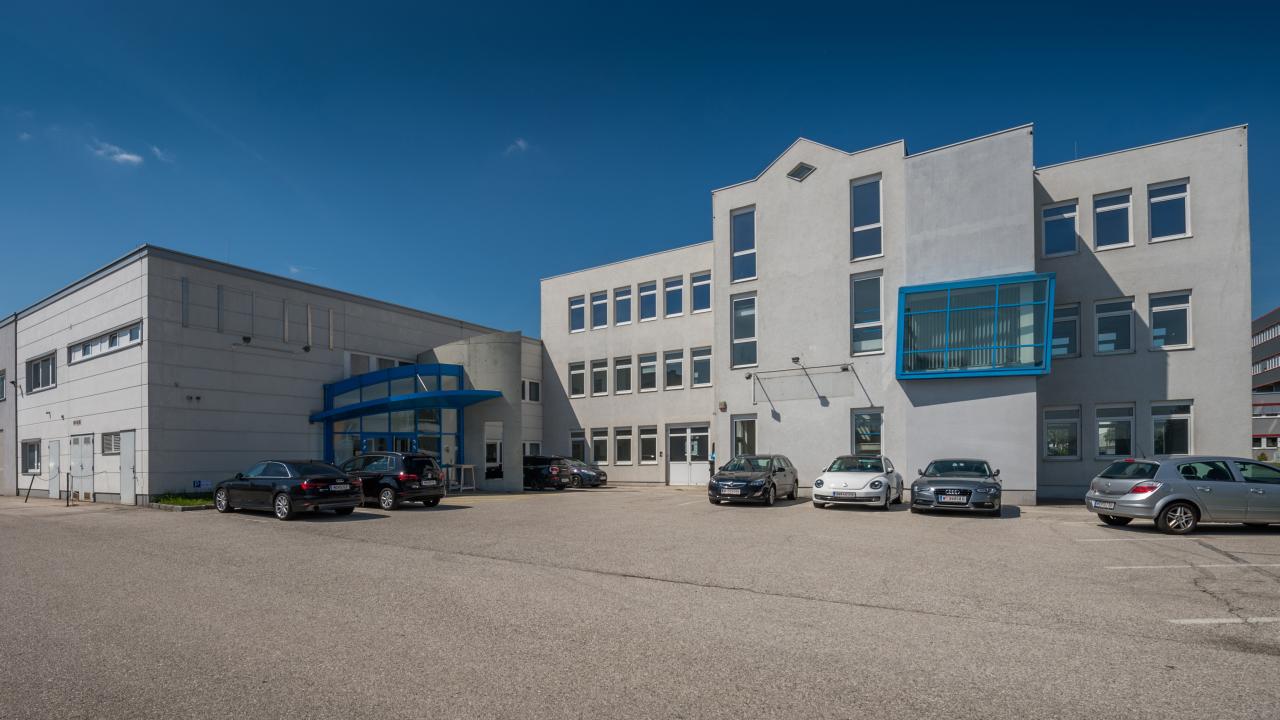 Außenansicht Mietobjekt M12 mit Parkplätzen und Autos vor Gebäuden im IZ NÖ-Süd