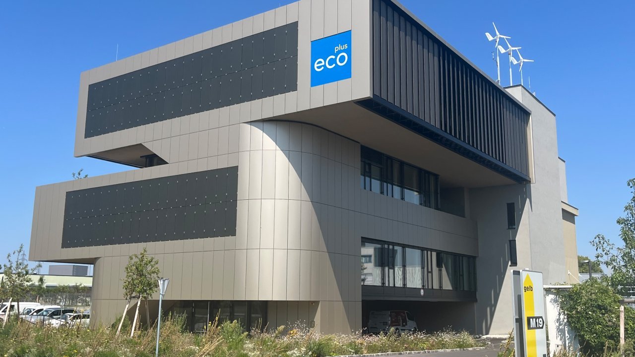 Außenansicht modernes Gebäude mit ecoplus Logo an Fassade und kleinen Windrädern am Dach