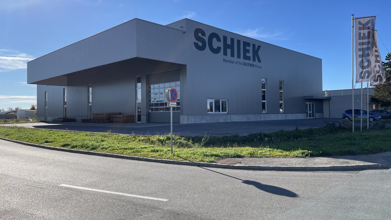 Außenansicht eines Bürogebäudes mit Firmenaufdruck, Parkplatz und Fahnen