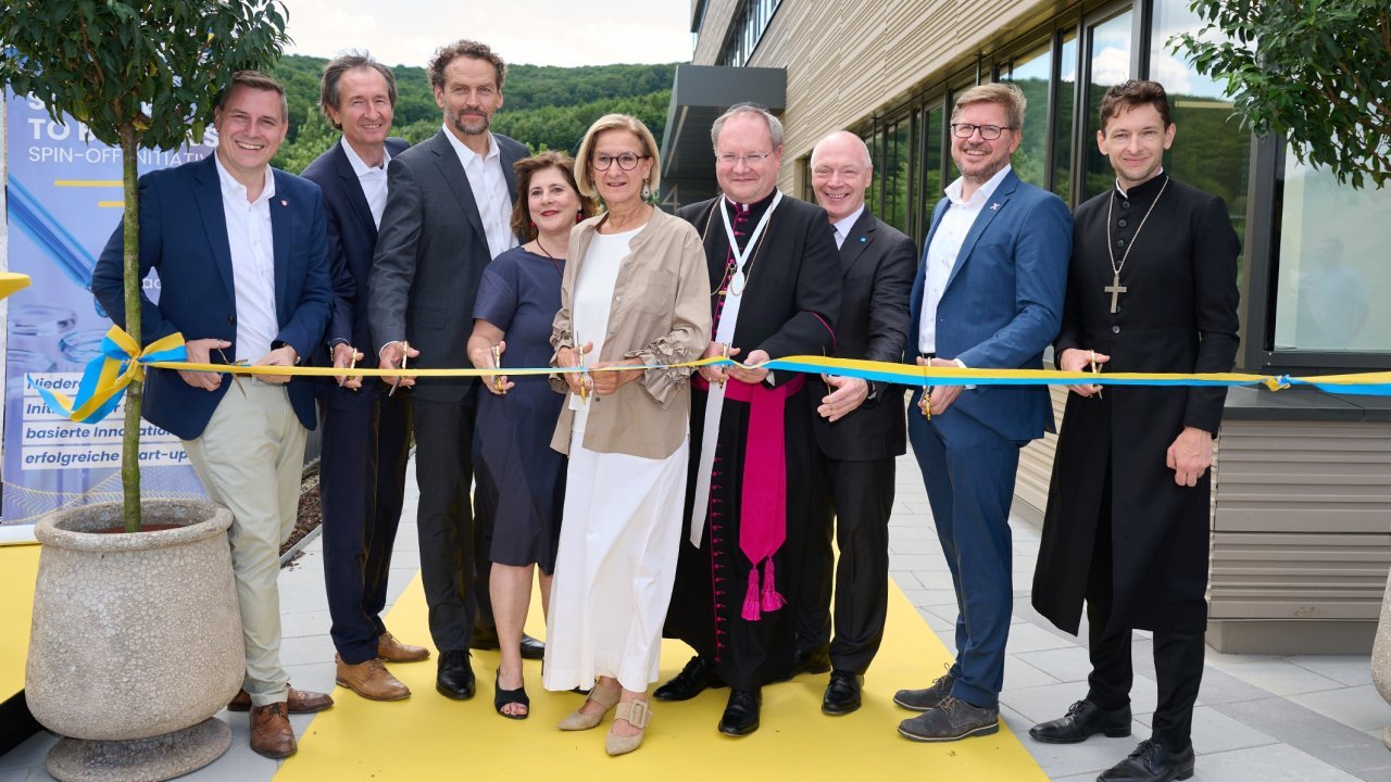 neun Personen stehen nebeneinander und schneiden ein blau-gelbes Band durch