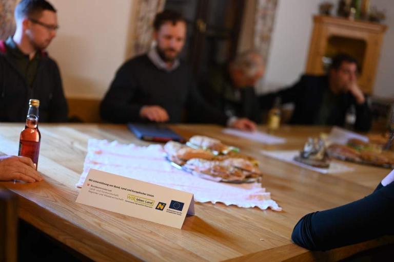ein Tisch mit einem Aufsteller und im Hintergrund sitzen Personen