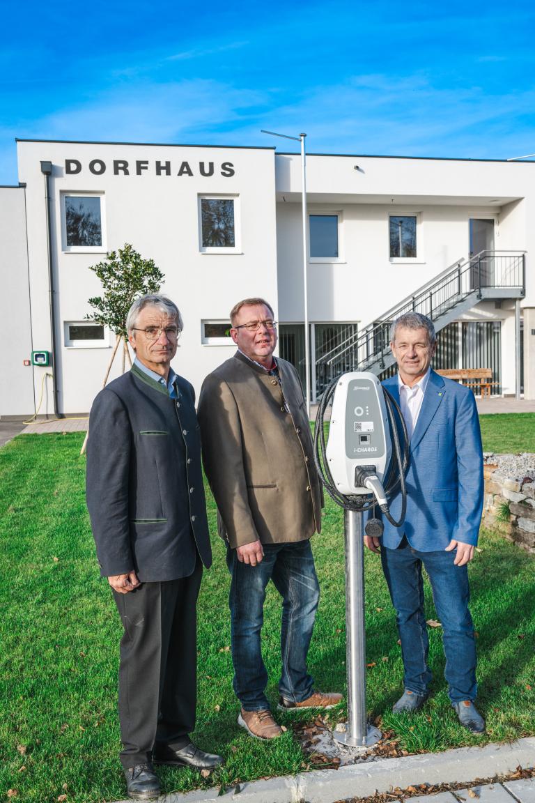 drei Personen stehen nebeneinander und präsentieren eine E Tankstelle