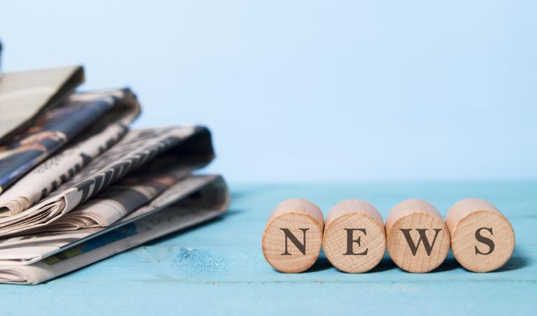 Stapel Zeitungen links und rechts kleine Holzsteine mit News-Schriftzug
