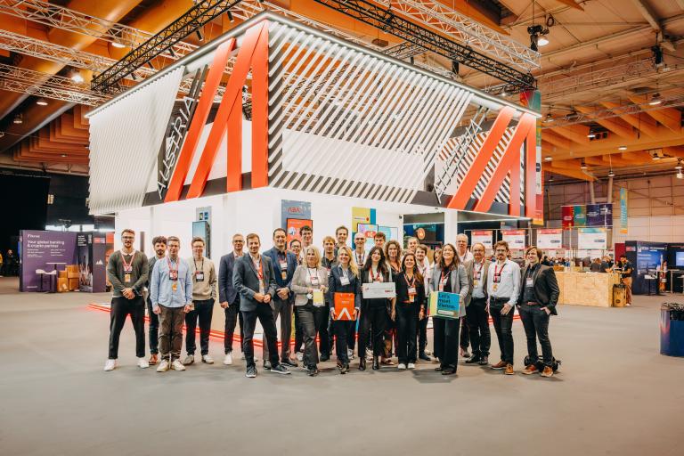 Approximately 30 people are standing in an exhibition hall in front of a booth