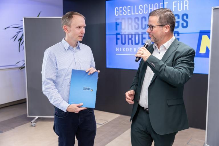 Verleihung von einer Urkunde von einem Moderator an einen Forscher