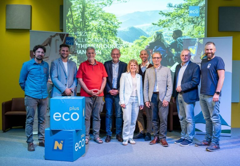 Acht männer und eine Frau stehen auf einer Bühne mit ecoplus Würfel