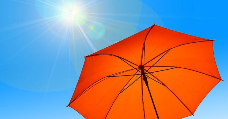 Oranger Sonnenschirm vor blauem Himmel mit Sonne