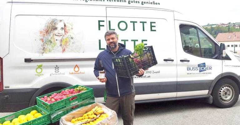 Mann mit Lebensmittelkiste steht vor kleinem Liefervan