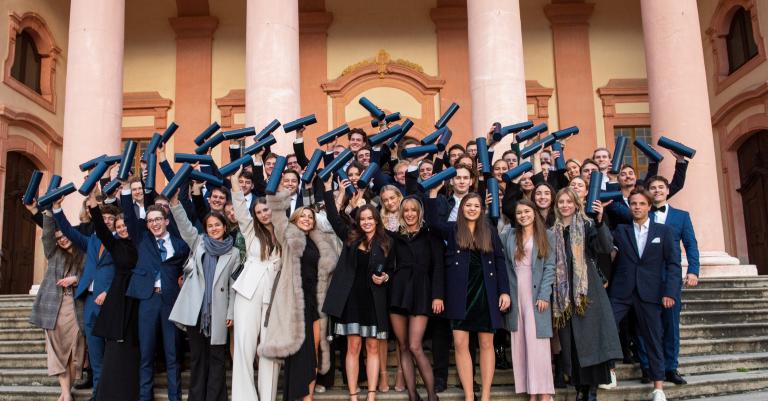 Gruppenfoto von Studierenden bei ihrem Abschluss: alle halten schwarze Rolle in ihren Händen
