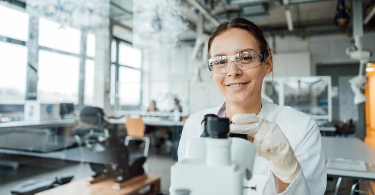 Frau mit Schutzbrille beim Mikroskopieren