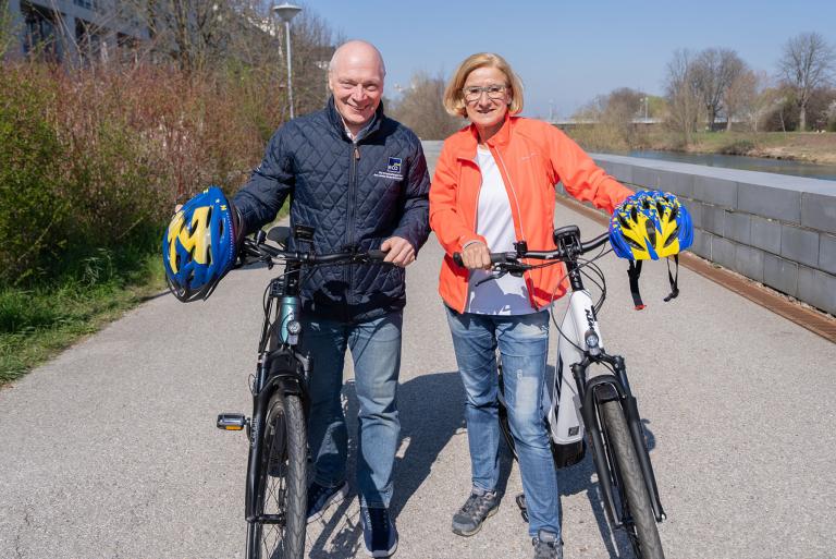 Mann und Frau mit 2 Fahrrädern und blau-gelben Helmen