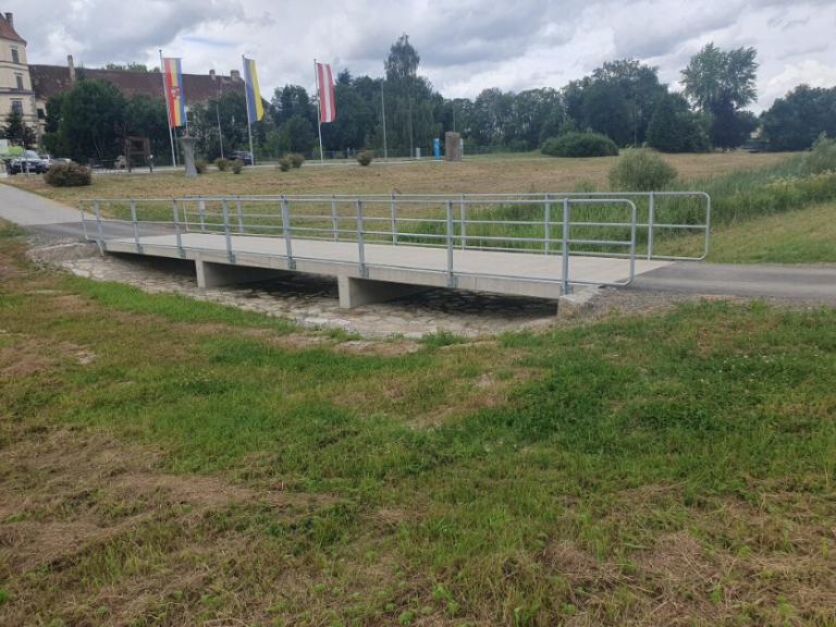 ein Radweg und eine Brücke verlaufen durch eine Wiese