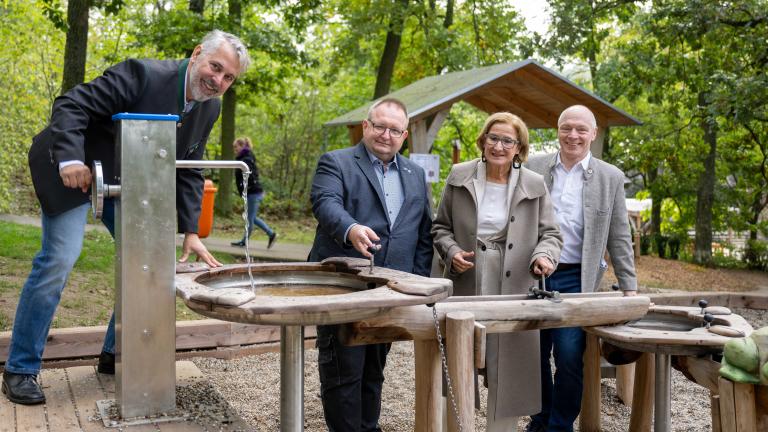 vier Personen stehen vor einem Wasserbrunnen und lachen in die Kamera