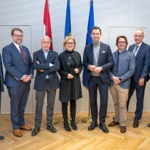 acht Personen stehen nebeneinander vor drei Flaggen