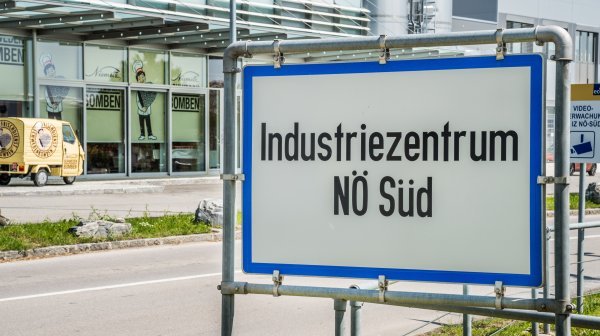 Ortschild Industriezentrum NÖ-Süd mit Firmengebäude im Hintergrund