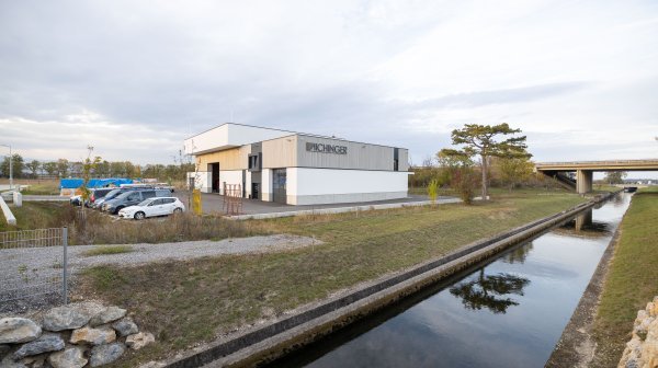 Firmengebäude Tischlerrei Aichinger neben offenen Wasserkanal und Föhre
