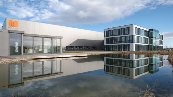 Modernes graues Firmengebäude mit orangen M auf der Fassade spiegelt sich in See