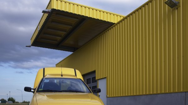 Gelbes Postgebäude mit Postauto davor