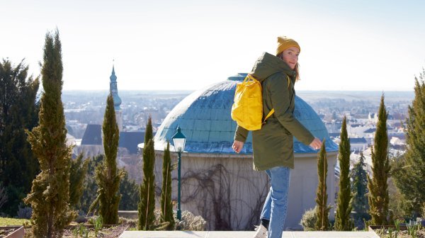 Dame mit gelbem Rucksack und schmalen hohen Bäumen 