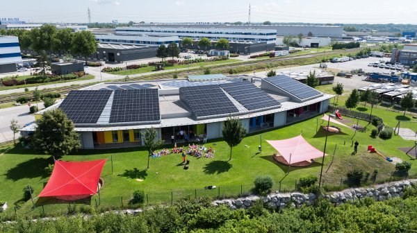 Drohnenansicht IZIBIZI mit Photovoltaik-Dach, Garten und Kindergruppe im Freien aus der Ferne