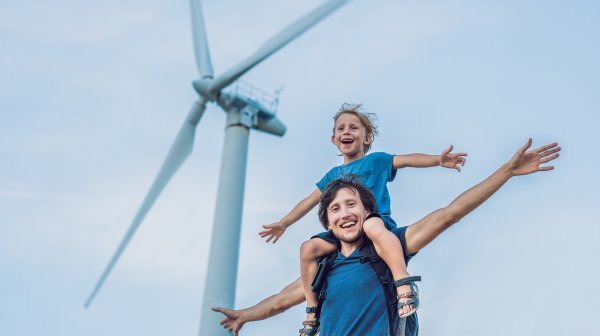 Mann mit Kind auf den Schultern und ein Windrad im Hintergrund