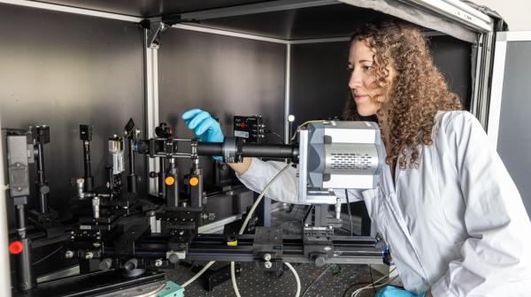 Forscherin in weißem Mantel und mit türkisen Handschuhen bedient ein elektronisches Gerät für präzische Messungen