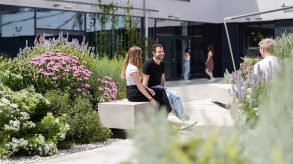 Studenten der FH Tulln sitzen vor dem Gebäude im Freien umgeben von Blumenschmuck